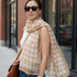 A woman wearing a lightweight beige and cream checkered scarf, paired with sunglasses and carrying a brown bag.