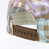 A cap featuring a colourful patterned fabric and an adjustable brown strap at the back, along with a logo.