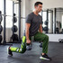 A man in grey shirt and green active pants performs lunges with dumbbells in a gym setting.