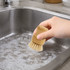 A bamboo kitchen dish brush with natural bristles held above a sink filled with soapy water.