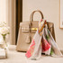 A handbag in a neutral tone with a floral twill weave square scarf tied around the handle.