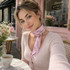A narrow pink chiffon scarf is tied elegantly around a person's neck, set against a café backdrop with flowers.