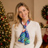 A satin long scarf in vibrant blues and greens, elegantly tied around the neck of a smiling model, set against a festive backdrop.