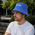 A blue reversible bucket hat with a logo, featuring a contrasting floral lining, worn by a model outdoors.
