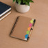 A brown spiral notebook sits on a wooden surface, accompanied by a pen and vibrant sticky notes in various colours.