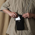 A minimalist black crossbody phone bag being held by a person, with a phone partially inserted into its pocket.