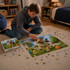 A boy assembling a colourful jigsaw puzzle featuring a dog in a vibrant outdoor scene, with a gift box beside him.