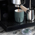 A drink bottle in a muted green colour with a ceramic liner, placed near an espresso machine on a black countertop.