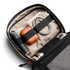 A tech kit featuring a grey exterior, tan interior, drink bottle, earphones, charging cables, and a pen.