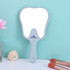 A tooth-shaped face mirror in light grey with a handle, set against a pastel blue background.