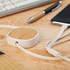 A USB charger cable with a bamboo and white casing, placed on a wooden surface alongside a pen and smartphone.