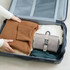 A grey folding travel toiletry bag positioned among folded sweaters in a blue suitcase.