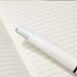 A white pen rests on a lined notebook page, featuring a sleek design and minimalistic style.