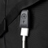 A close-up of a black backpack with a USB charging port and cable attached. It features a textured strap.