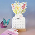 A floral desk calendar with illustrations of tulips and daffodils, featuring a stand. Pink and green colours are prominent.