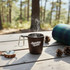 A drink bottle in dark brown with a logo, steam rising from its opening, placed on a wooden table outdoors.