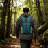 A large packable camping backpack in teal is worn by a person walking along a forest path.