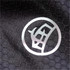 A close-up of a black textured fabric featuring a circular logo. The texture resembles a honeycomb pattern.