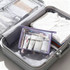 A clear, purple travel cosmetic bag filled with toiletries, placed inside a suitcase alongside folded clothes.