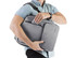 A grey backpack is being carried by a person, with a visible pocket and a logo. The person is wearing a light blue shirt.