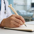 A cream-coloured pen shaped like a bone held by a person in a white coat, writing in a notebook.