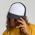 A black and white trucker cap featuring a flat brim and mesh back, worn by a person with long, curly hair.