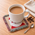 A drink bottle rests on a festive jacquard coaster featuring Santa, with coffee beans and a spoon nearby.