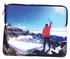 A neoprene laptop sleeve featuring a mountain landscape and a person in a red jacket, with a branded logo.