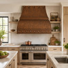 Antique hammered copper range hood in a rustic transitional kitchen with white oak cabinets and pale stone