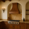 Designer copper range hood with a Gothic apron in a California Mission style kitchen featuring warm woods, stucco tones, and handcrafted details