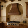 Hand-hammered designer copper range hood with a Gothic apron in a Spanish style kitchen featuring warm tones, tile accents, and rustic wood elements