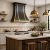 Zinc range hood with brass straps, apron, and black crown molding in a contemporary Italian kitchen with limewash walls and warm wood cabinets