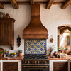 Scalloped dome copper range hood in a Spanish Colonial kitchen with plaster walls, Saltillo tile, and iron accents