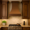 High ceiling wall mount copper range hood in traditional kitchen, tall hammered canopy with warm patina above classic cabinetry and stone backsplash