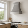 Zinc range hood with bell shaped design and satin finish in modern minimalist kitchen, smooth curved canopy above sleek cabinetry and clean architectural surfaces
