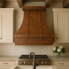 Custom copper kitchen hood in a farmhouse kitchen with rich copper tones, white Shaker cabinets, and a reclaimed wood beams