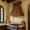 Spanish Colonial style kitchen featuring a 36-inch hammered copper range hood above the cooktop with warm wood cabinetry and stone backsplash