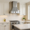 Architectural zinc range hood with flared canopy and crown detail in transitional kitchen, smooth zinc surface above balanced cabinetry and stone backsplash