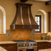 Decorative copper kitchen vent hood with silver vertical straps in Mexican Hacienda kitchen, hammered copper canopy above rustic beams and plaster walls