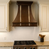 Decorative copper kitchen vent hood with silver vertical straps in traditional kitchen, hammered copper canopy above classic cabinetry and stone backsplash