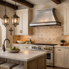 Brushed zinc range hood with crown shelf and dark trim in a Spanish Mediterranean kitchen