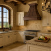 Decorative copper kitchen range hood in large Tuscan kitchen, hammered copper canopy with riveted straps and carved grapevine apron above stone surfaces
