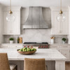 European bell-shaped zinc range hood in a transitional kitchen with clean cabinetry and natural stone counters