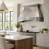 Handcrafted pewter range hood with Mexican design in rustic modern kitchen with lightn color stone tile backsplash and white marble countertops