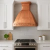 Modern kitchen with polished copper range hood and Rococo apron design, reflective canopy above range with clean cabinetry and stone surfaces
