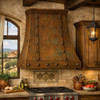 Handcrafted hacienda copper range hood with riveted straps in Tuscan kitchen with warm stone, rich patina and dark wood beems