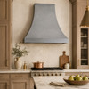 Smooth natural zinc bell hood in transitional warm kitchen with marble counters and brass accents