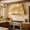 Tin range hood in Tuscan kitchen with rustic dark wood cabinets, travertine backsplash walls, terracotta tones and iron chandelier