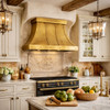 Riveted tin bell canopy range hood in French Country kitchen with painted cabinets, stone backsplash, aged brass
