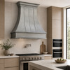 Natural zinc range hood with curved bell design in minimalist kitchen with flat-panel cabinetry and integrated appliances